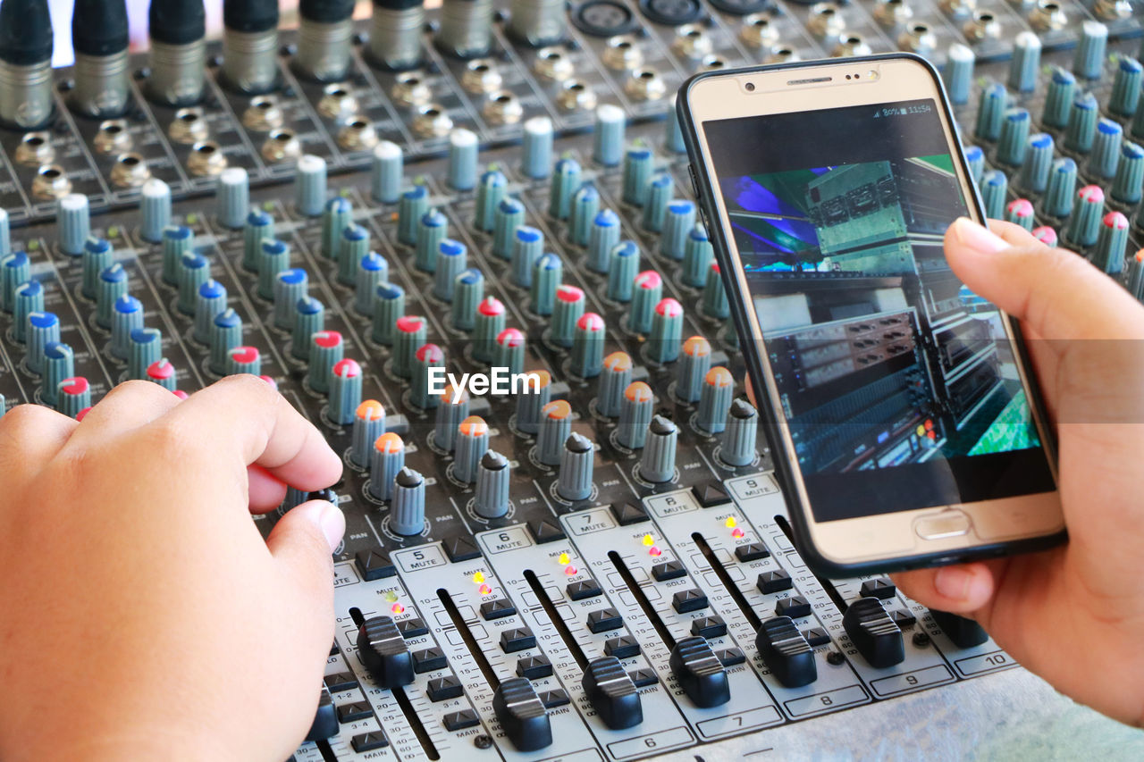 Person holding smart phone over sound mixer at recording studio