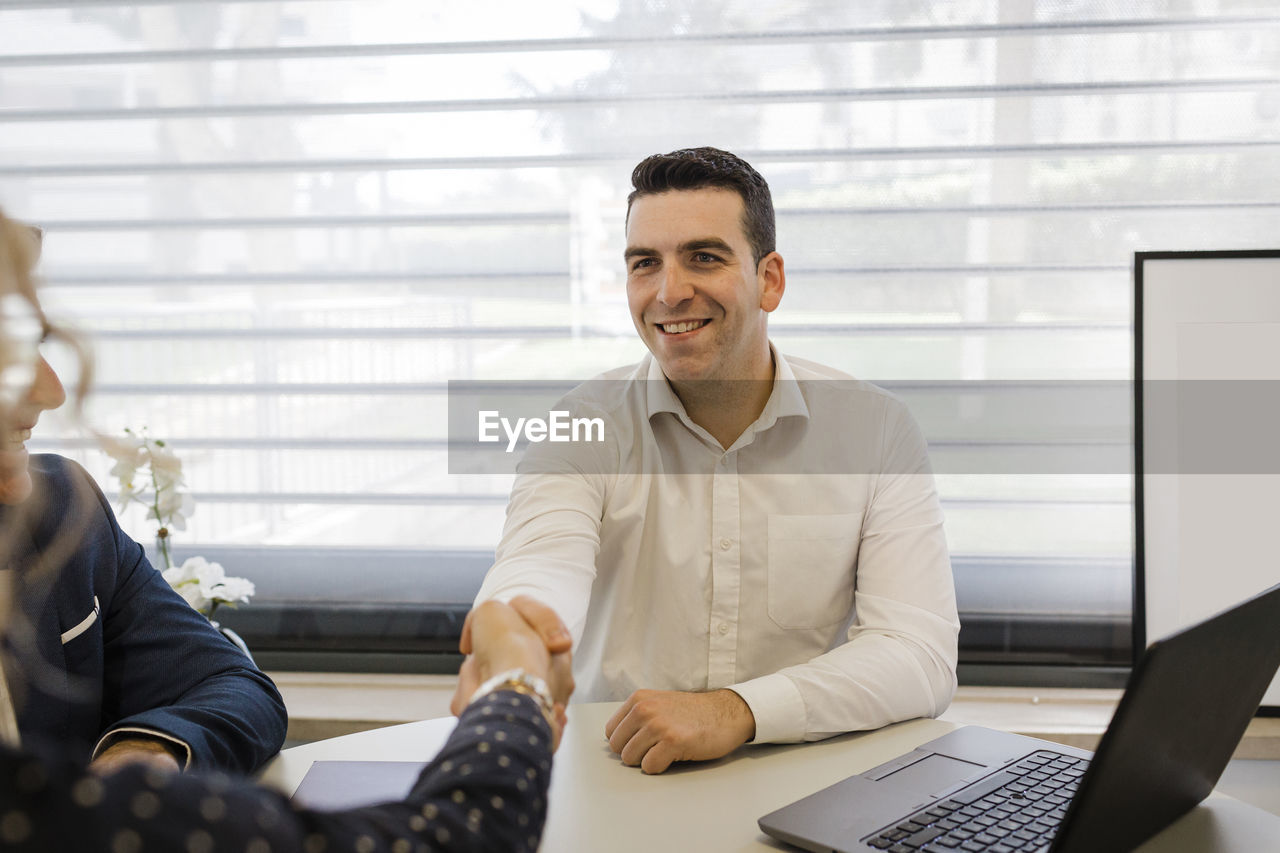 Happy businessman shaking hands with colleague at desk in office