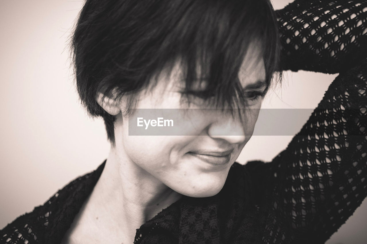 Close-up of mid adult woman with short hair looking away while standing against wall