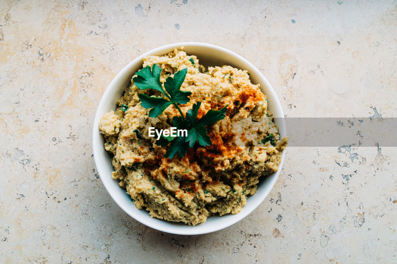 A bowl of hummus dip with green parsley on top