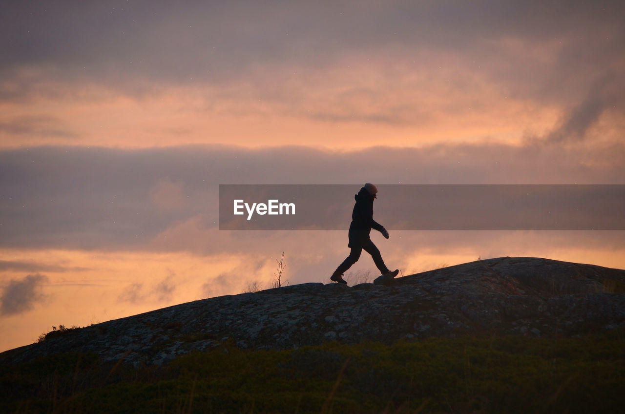 Woman walking on mountain against sky during sunset