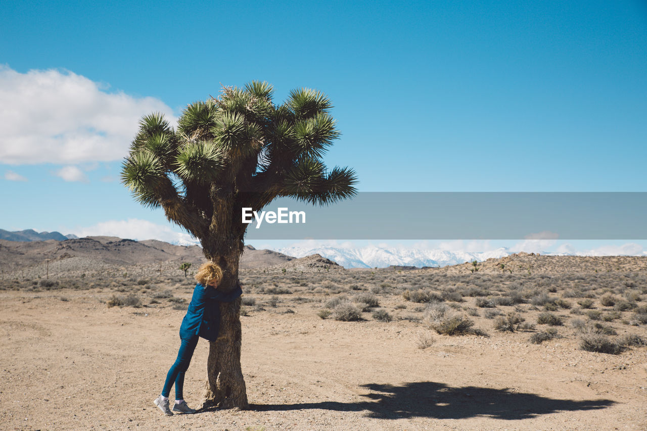 Woman hugging tree in desert against sky