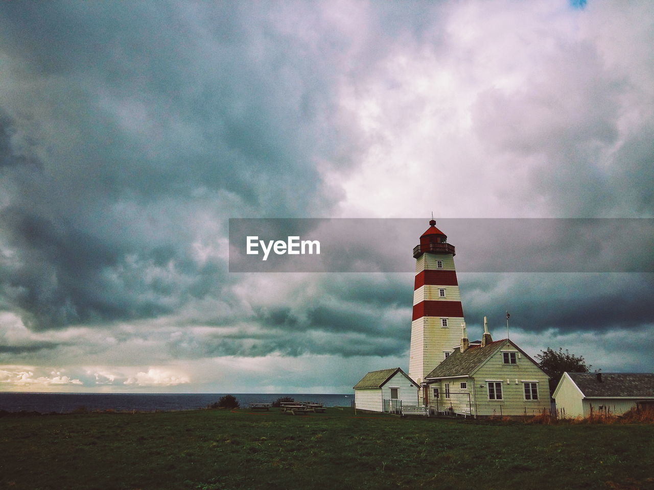 Houses and lighthouse on shore against cloudy sky