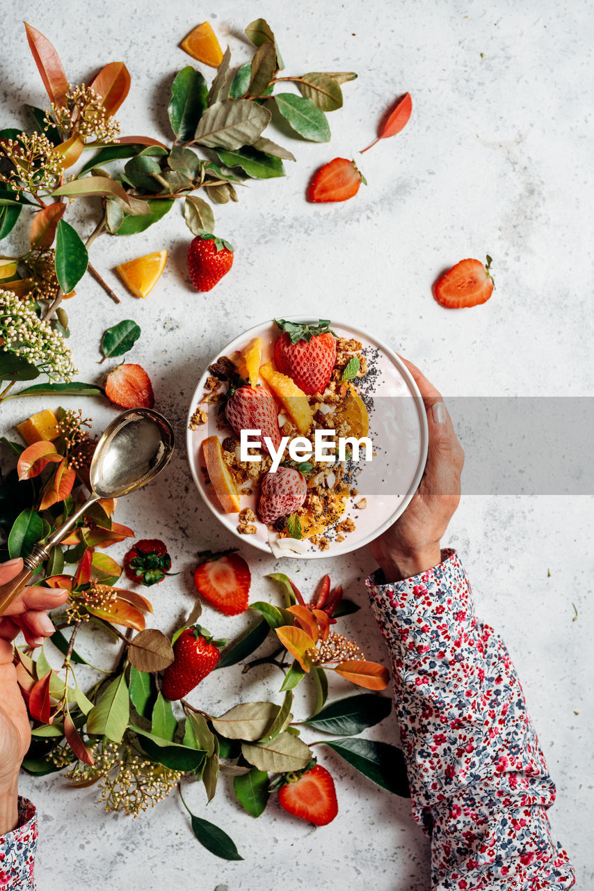 From above of unrecognizable female with smoothie bowl with fruits and berries sitting at table during breakfast in morning