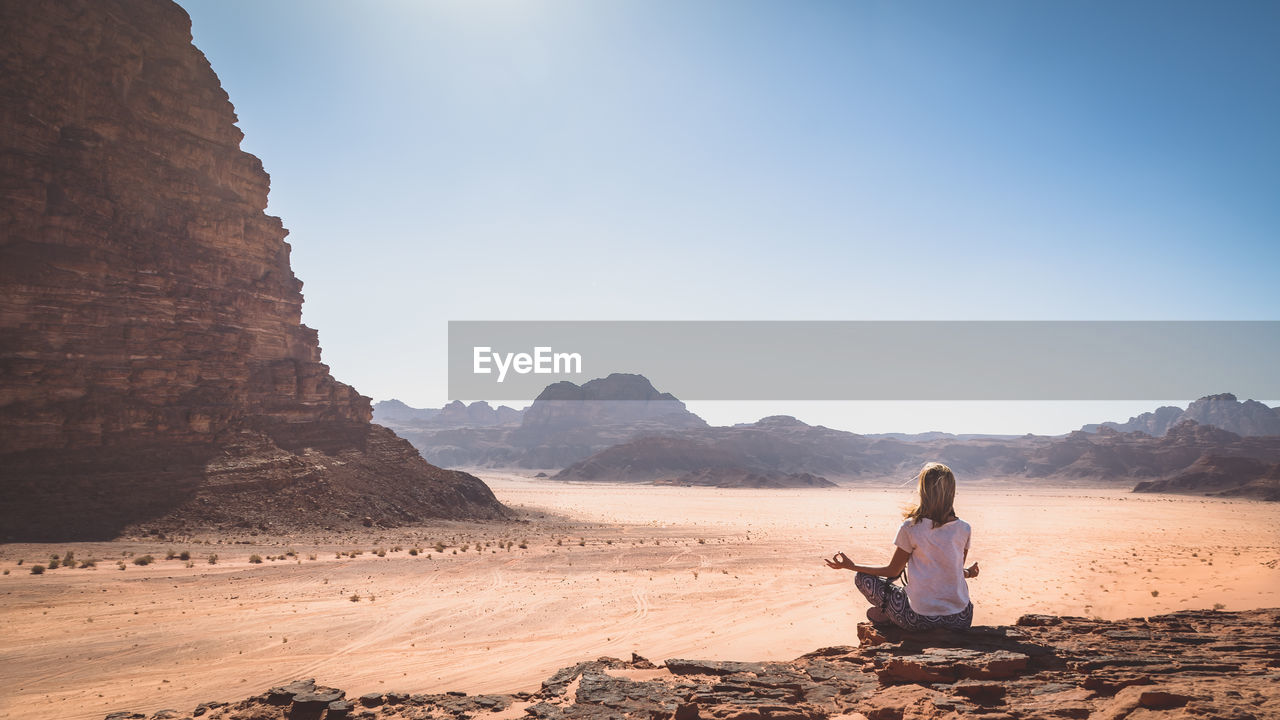 Woman meditating on landscape against clear sky