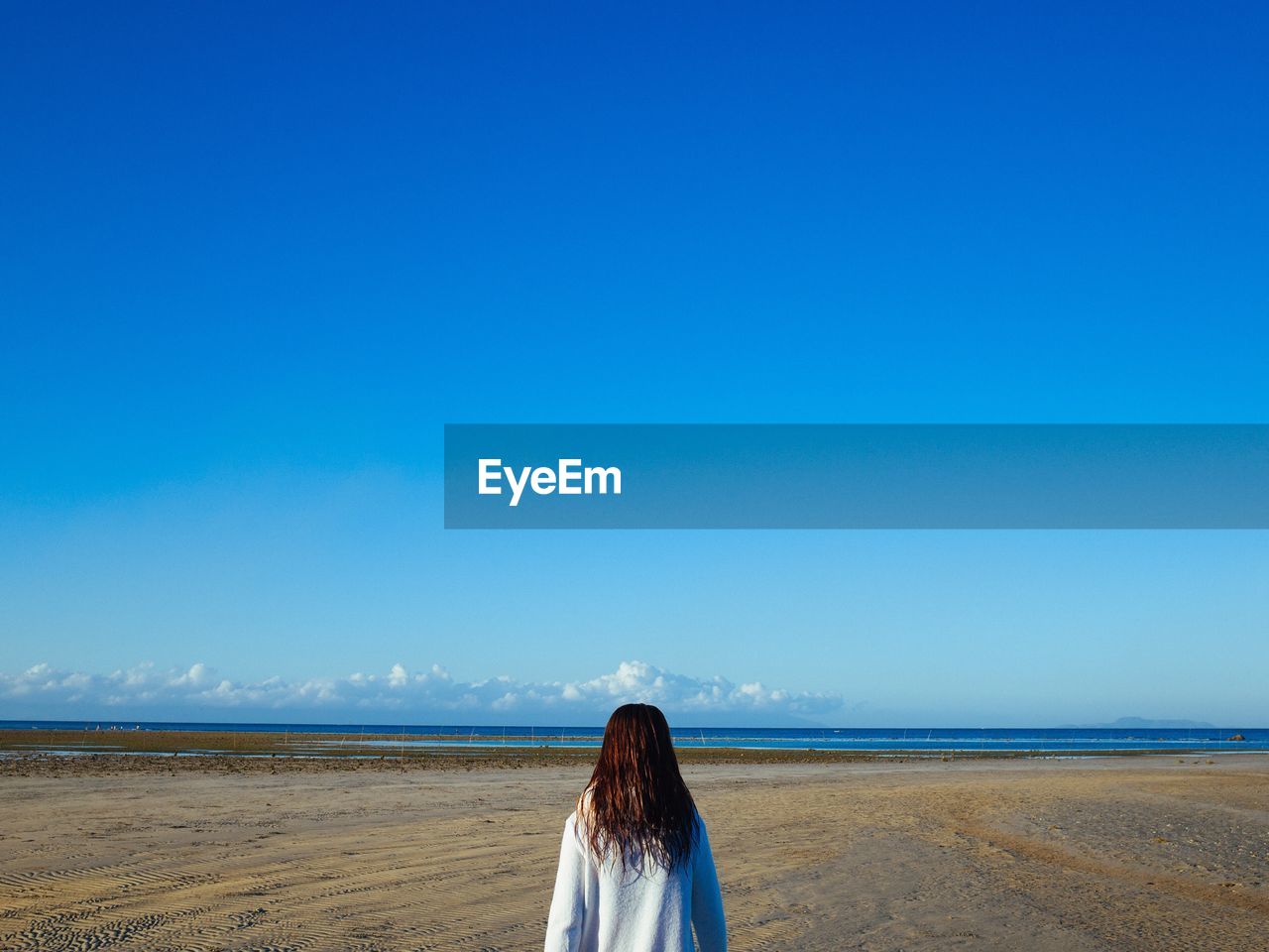 Rear view of woman standing at beach against blue sky