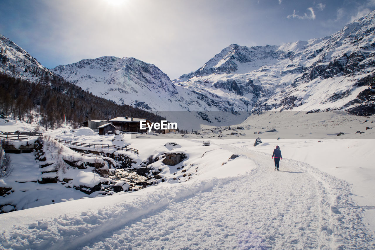 Woman walking on snowcapped mountain against sky