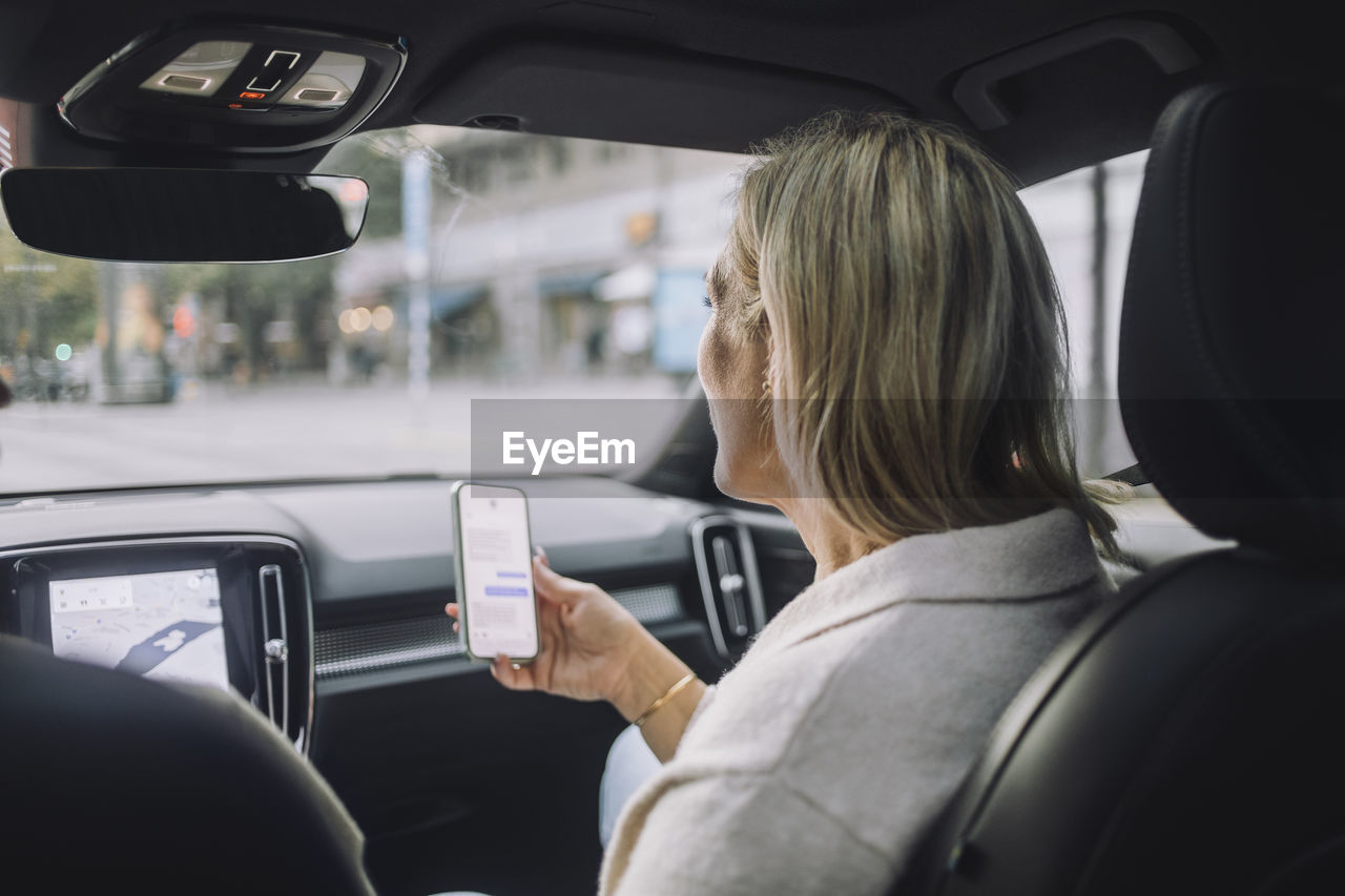 Mature woman using smart phone while sitting in front passenger seat