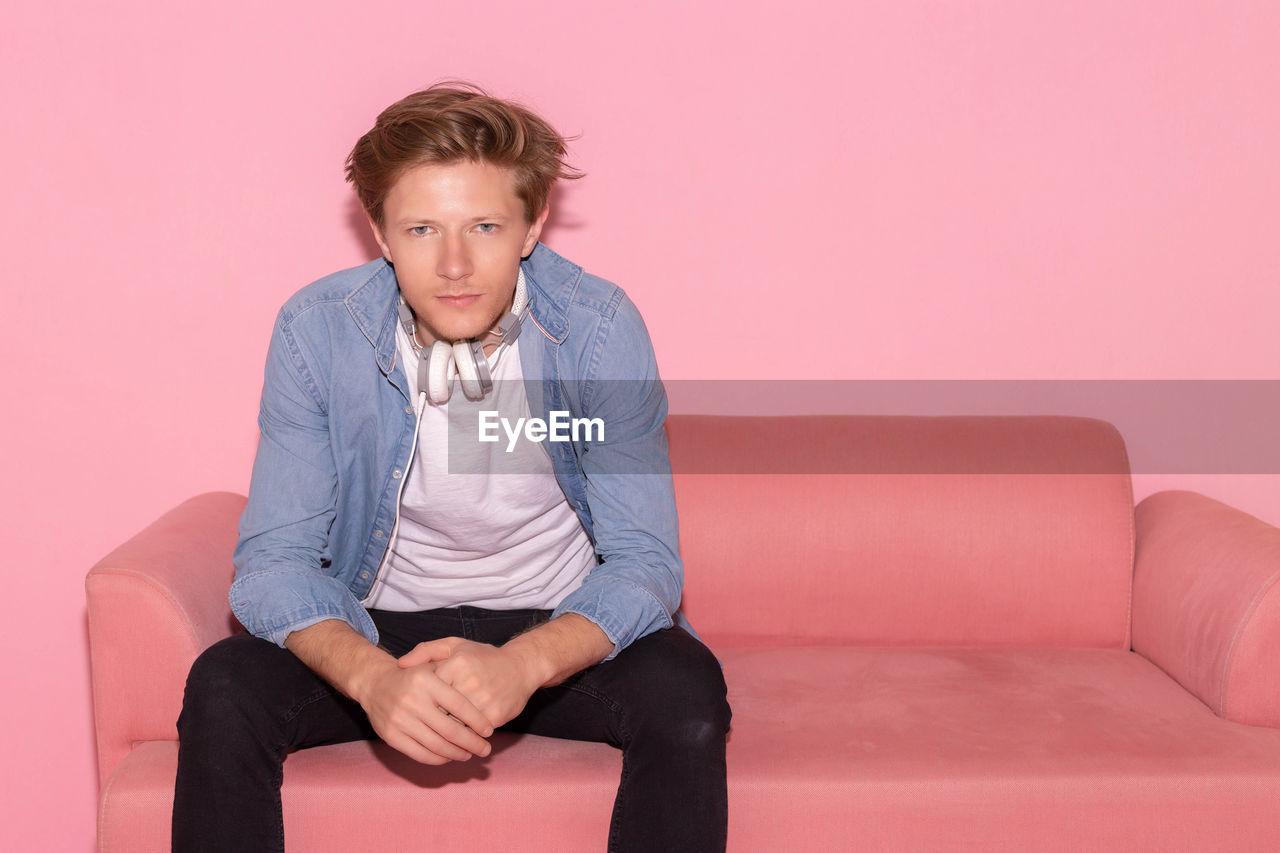 Portrait of man sitting on sofa against pink background