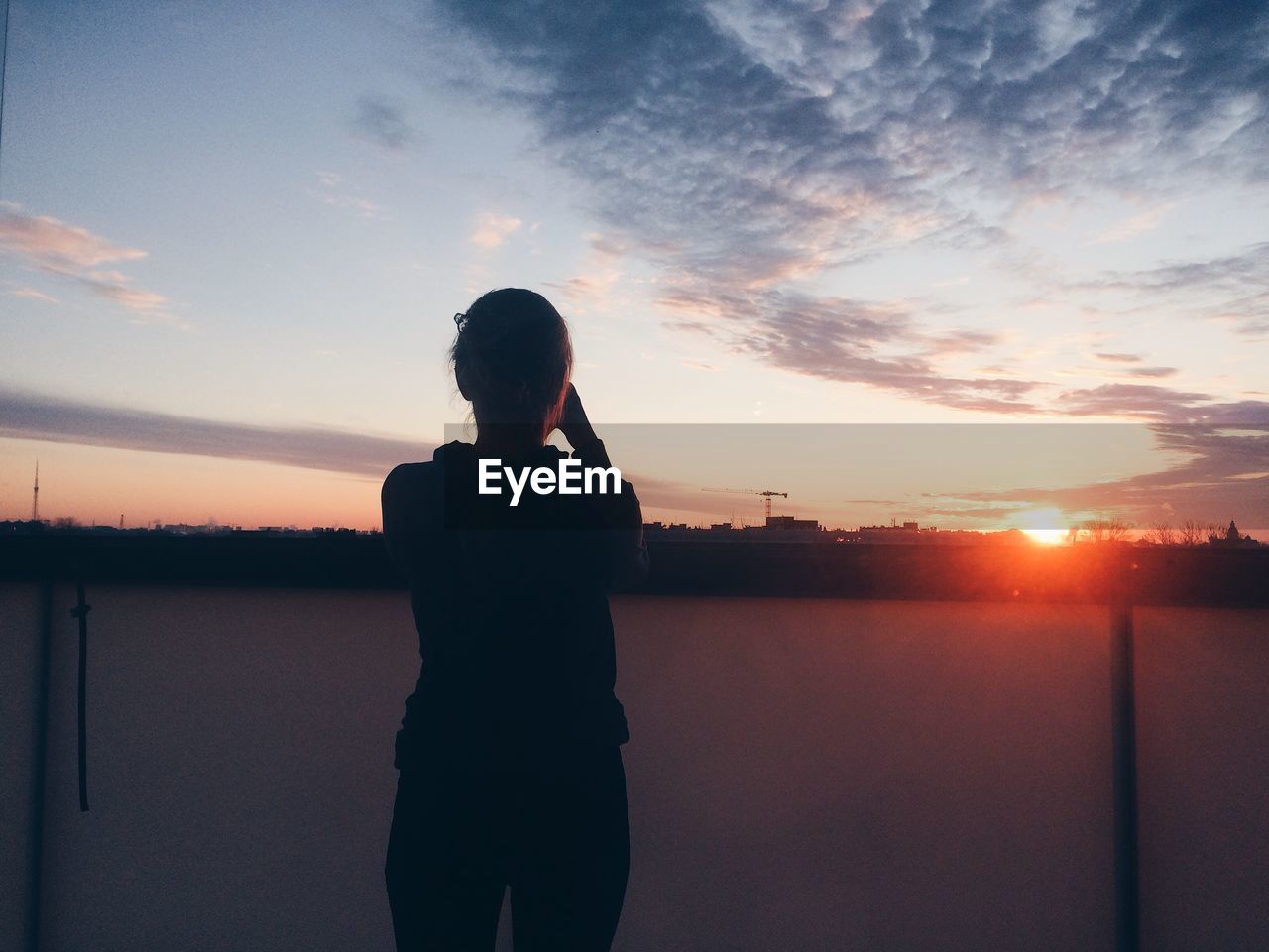 REAR VIEW OF WOMAN STANDING AGAINST SUNSET SKY