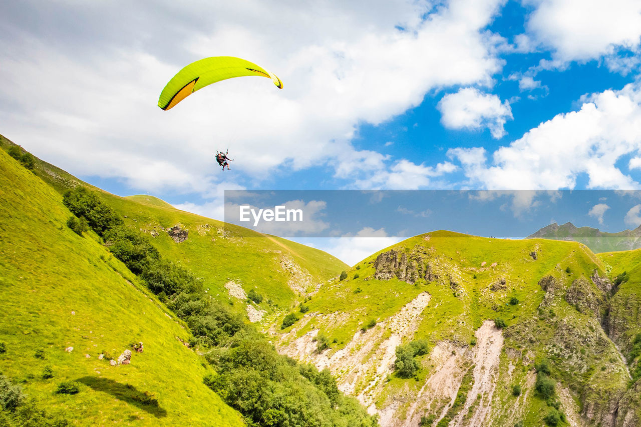 PERSON PARAGLIDING OVER GREEN MOUNTAIN AGAINST SKY