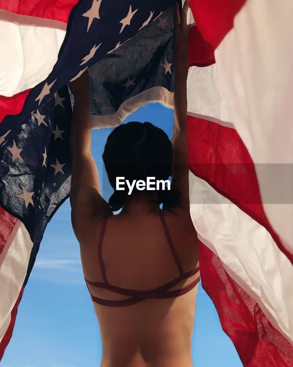 Rear view of woman standing with american flag at beach