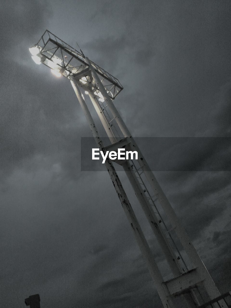 Low angle view of tall illuminated billboard tower against cloudy sky at dusk