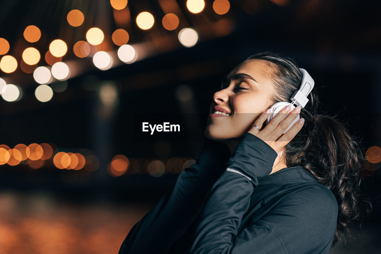 WOMAN LOOKING AWAY WHILE STANDING ON ILLUMINATED MOBILE PHONE