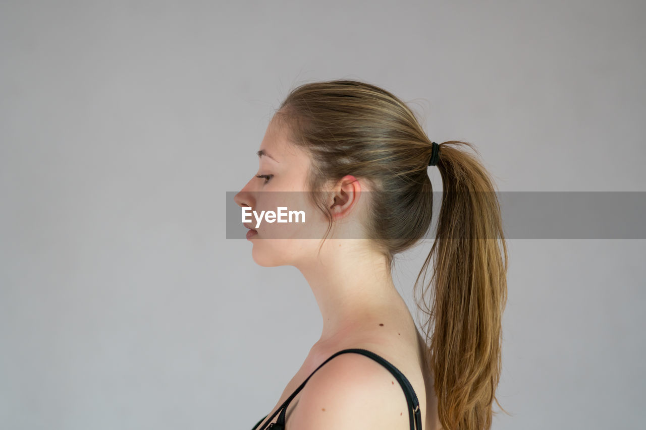 SIDE VIEW PORTRAIT OF A YOUNG WOMAN AGAINST WHITE BACKGROUND