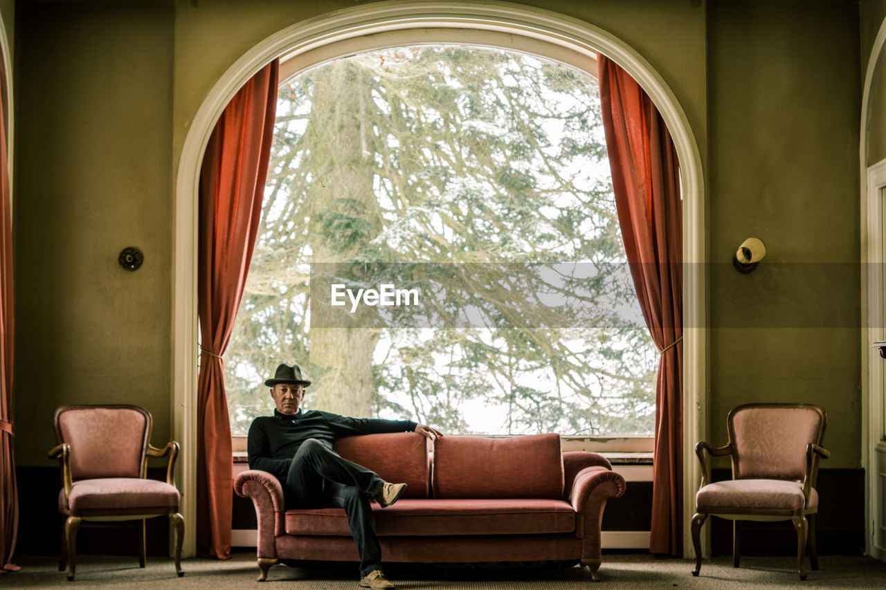 Mature man sitting on sofa against window at home during winter