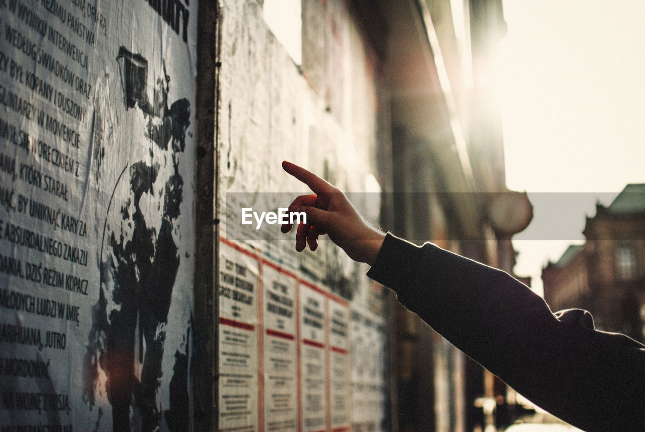 Cropped image of person pointing at sign board on building