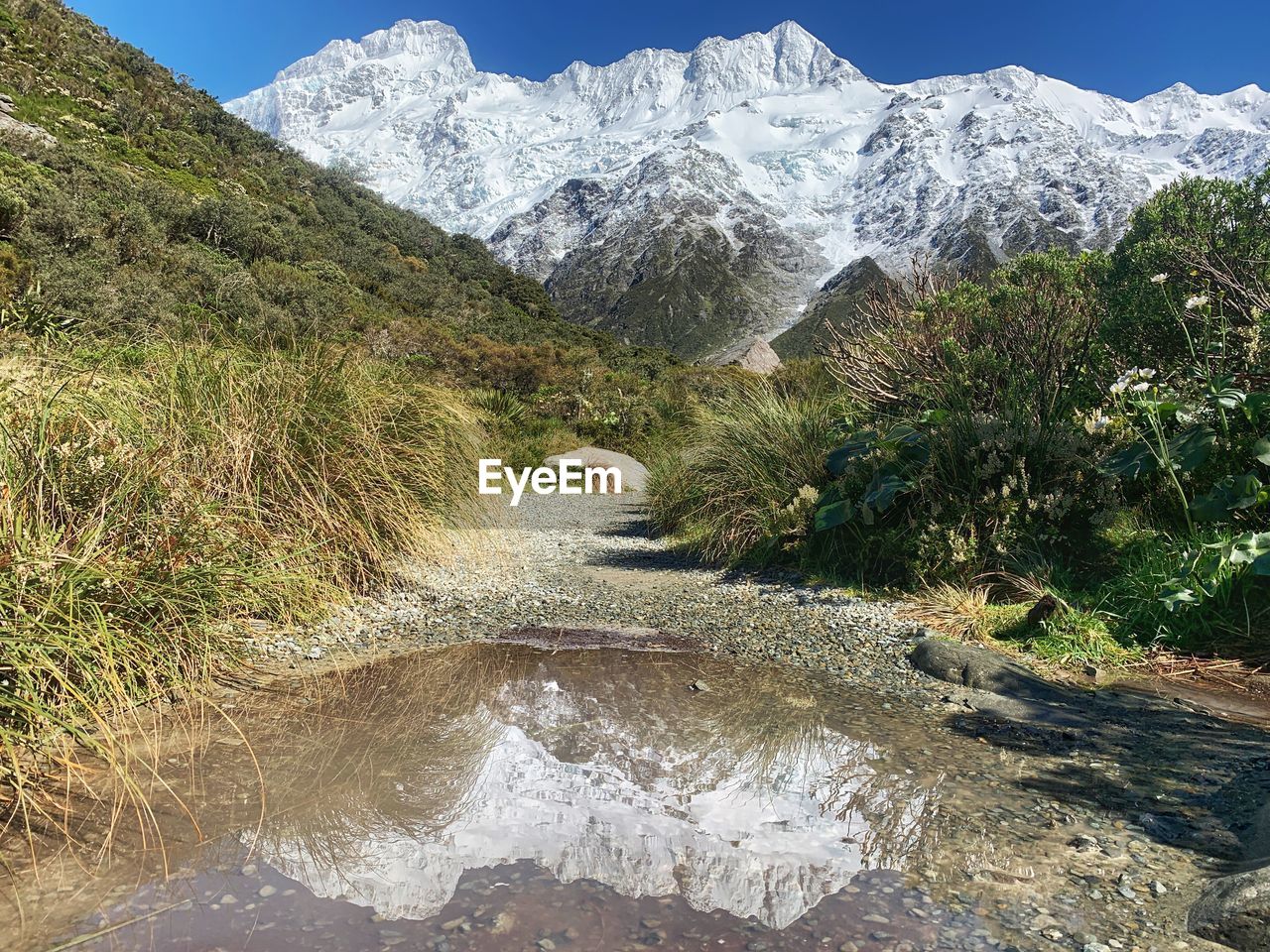 Scenic view of stream by snowcapped mountains against sky