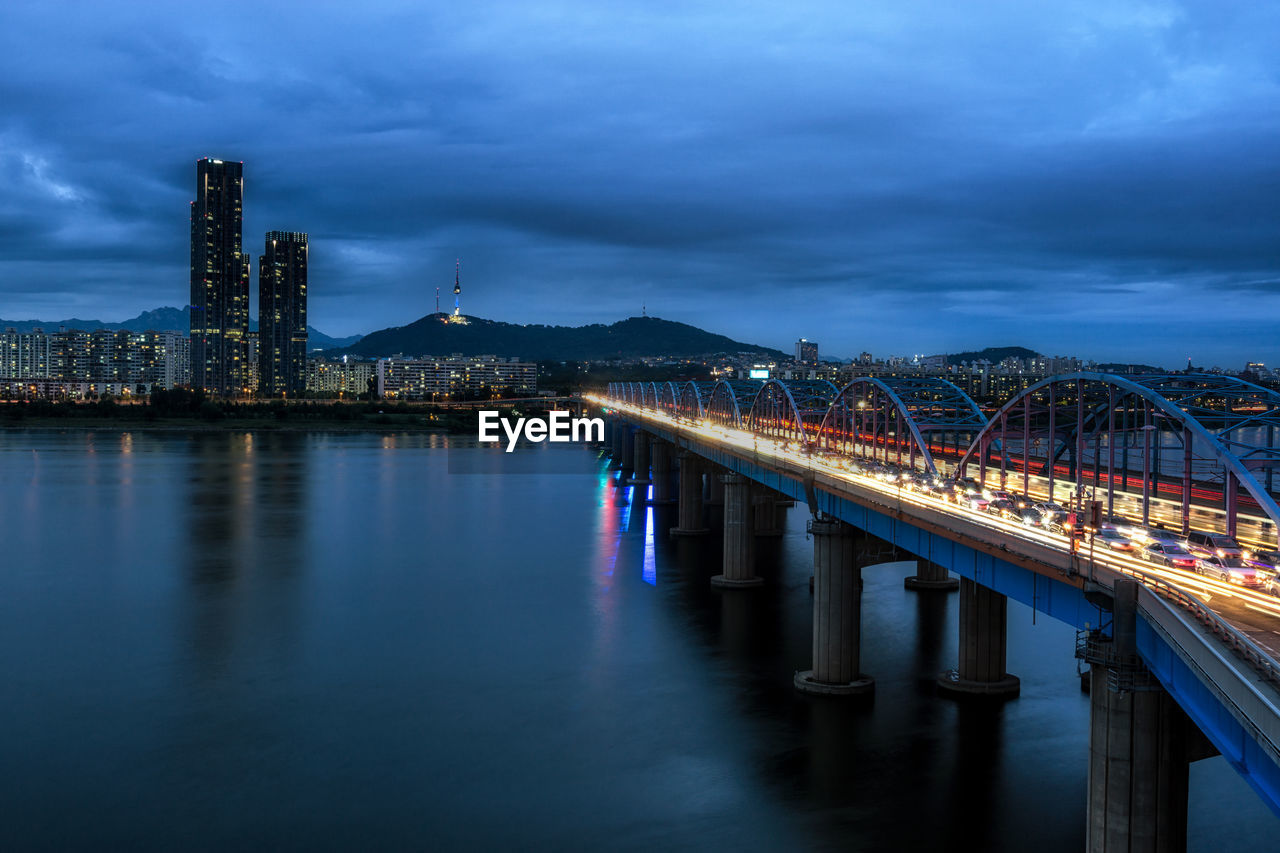 Illuminated bridge over river against sky at night