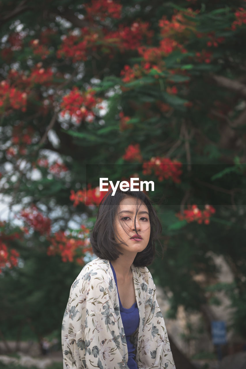 PORTRAIT OF BEAUTIFUL YOUNG WOMAN STANDING AGAINST TREES