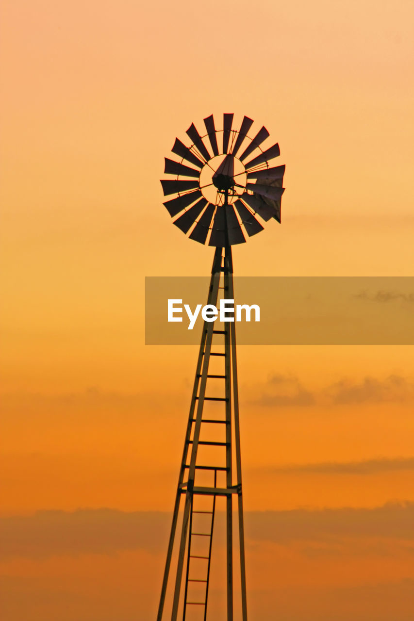 Low angle view of silhouette traditional windmill against orange sky