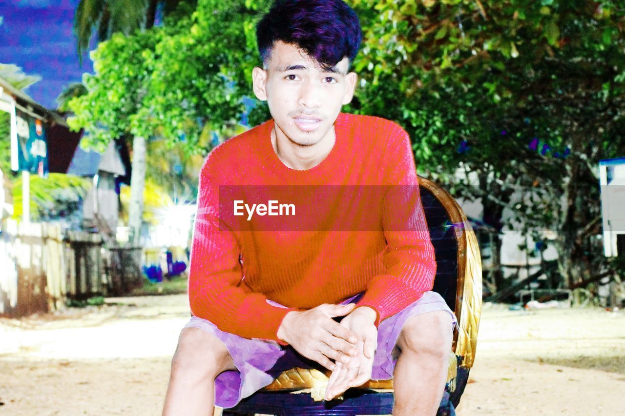 PORTRAIT OF YOUNG MAN SITTING ON WALL OUTDOORS