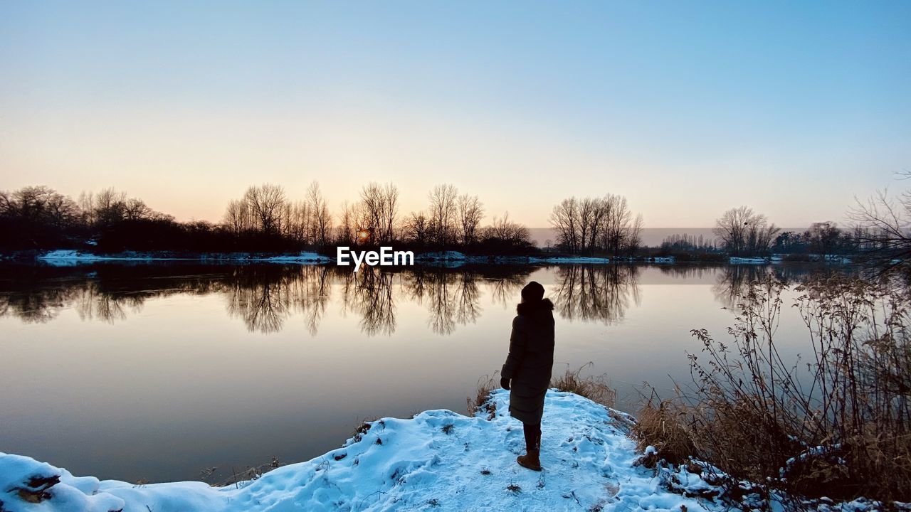 Full length of woman standing by lake against sky during winter