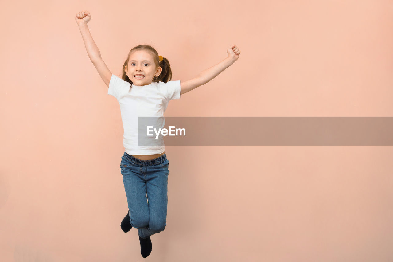 full length of young woman with arms raised standing against white background