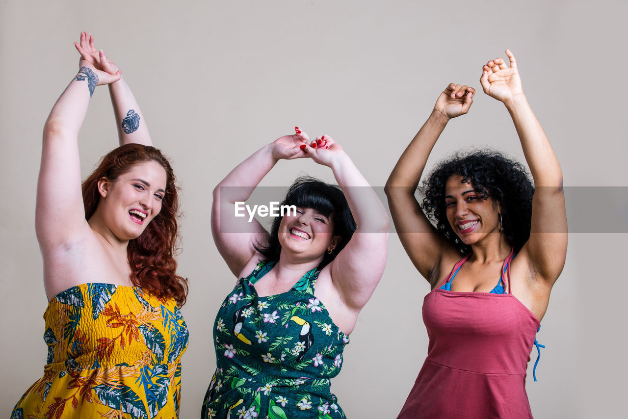 Portrait of smiling young women with arms raised against colored background