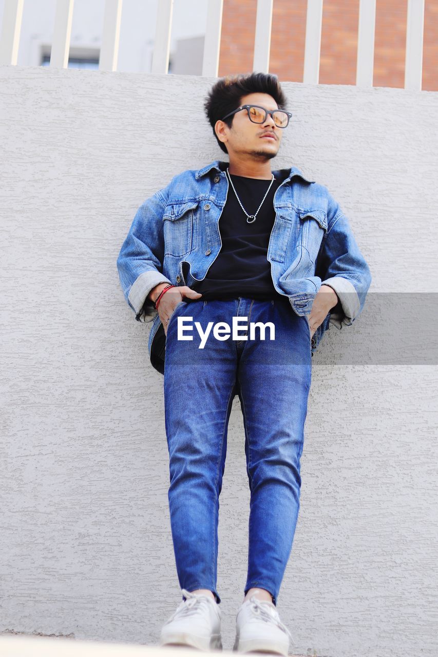 FULL LENGTH PORTRAIT OF A YOUNG MAN STANDING AGAINST WALL