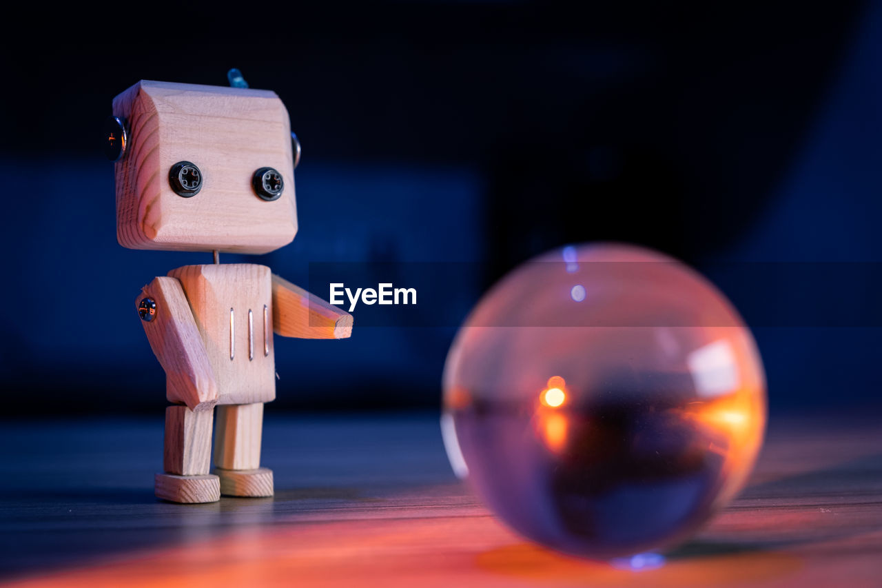 A small wooden toy robot looks at a magic glass ball in the dark. wallpaper, blured background. 