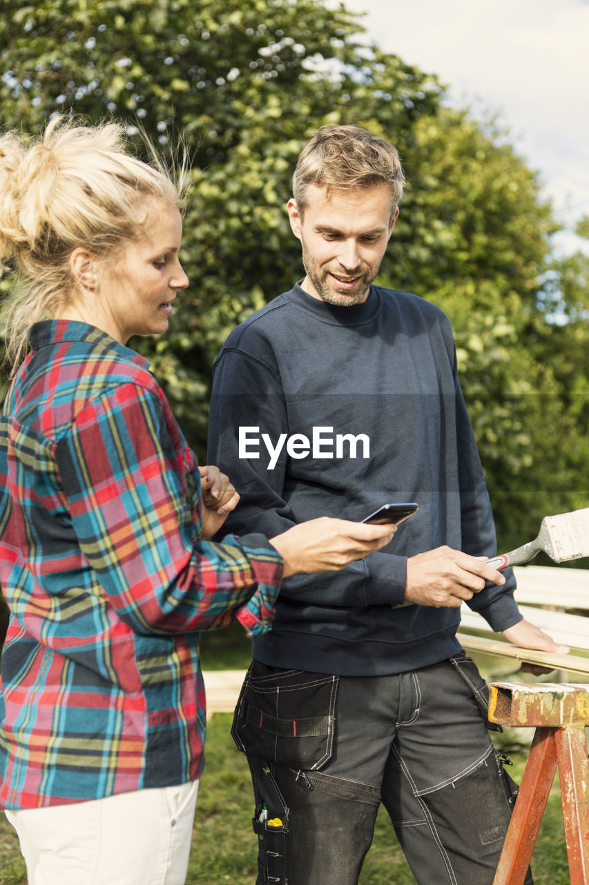 Woman showing phone to male worker while working at farm