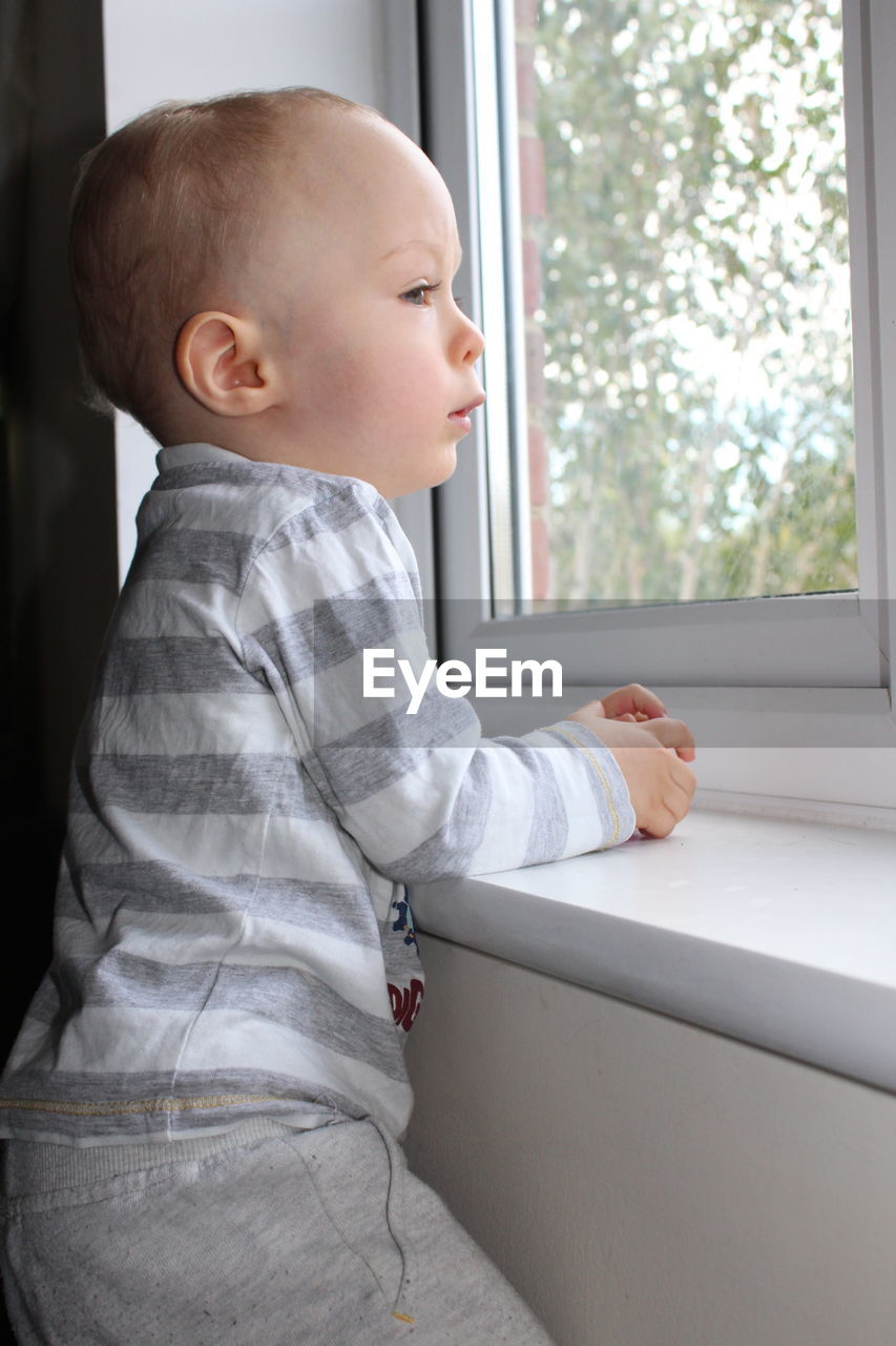 Side view of cute baby boy looking through window