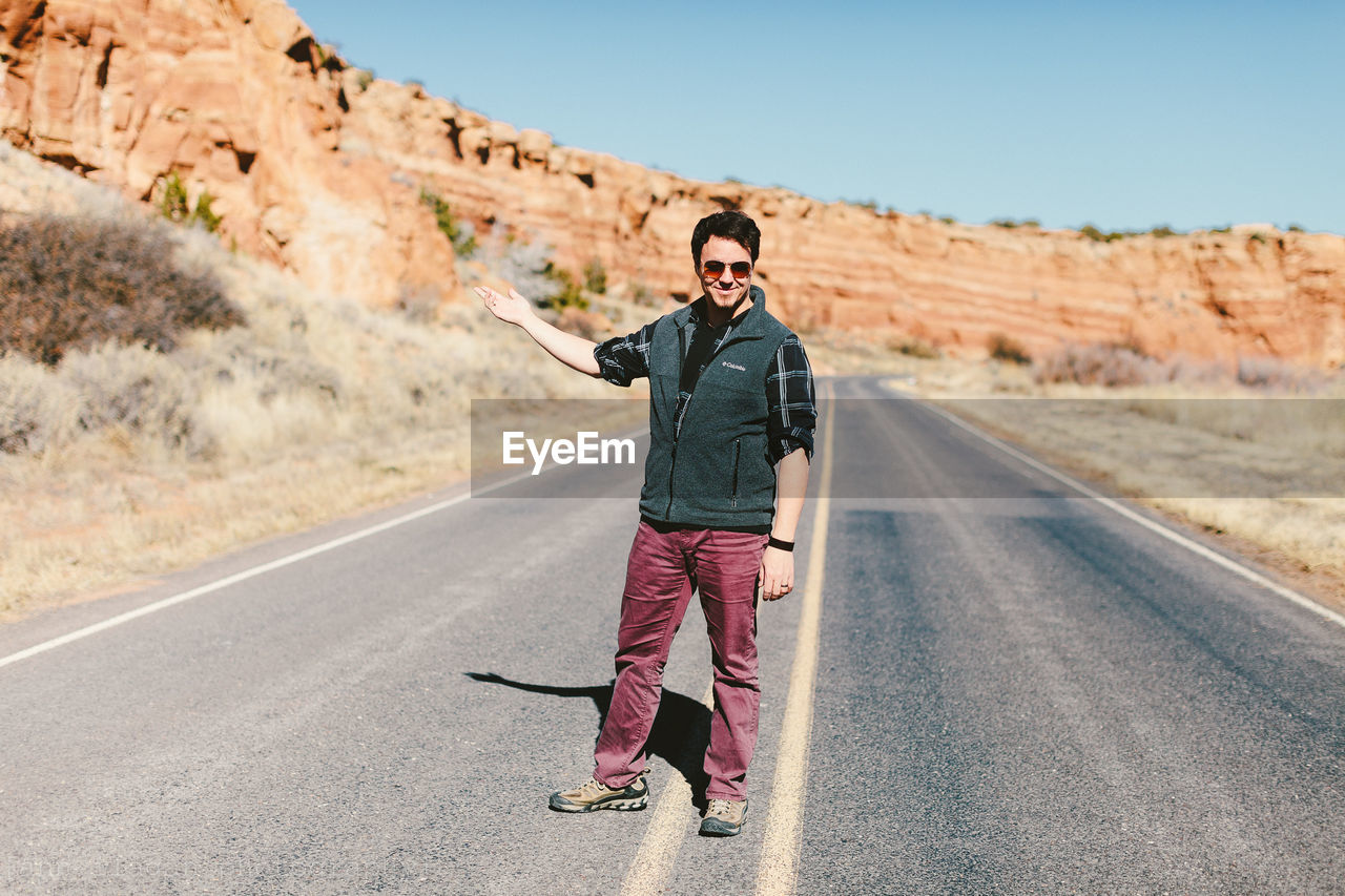 Full length of smiling man gesturing while standing on road by rock formations