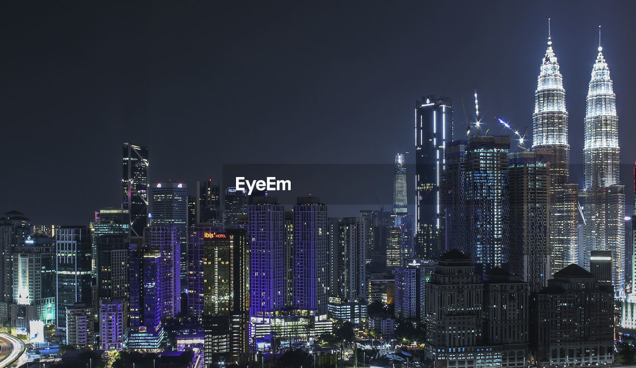 Illuminated modern buildings in city against sky at night