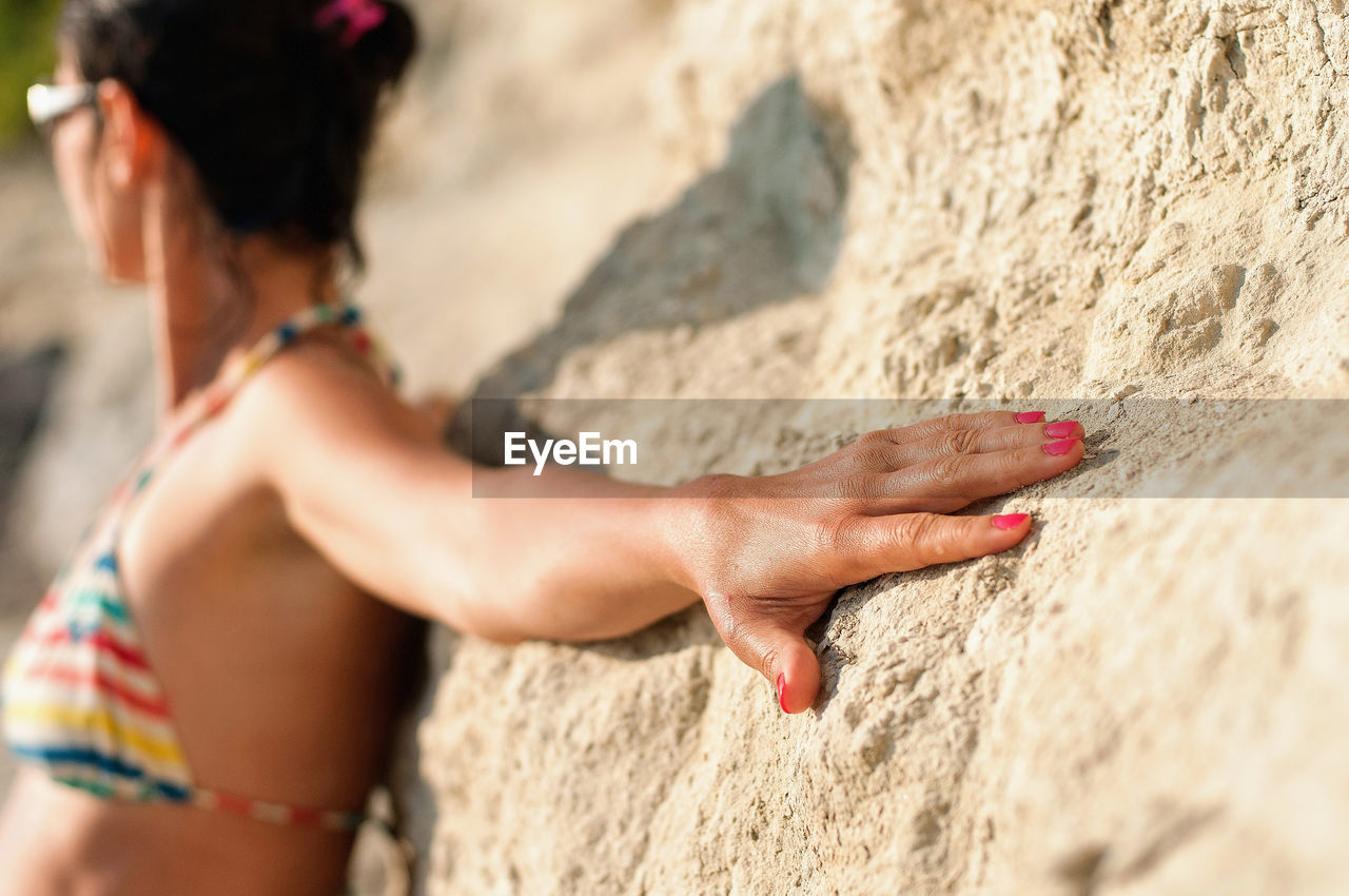 Woman wearing bikini while leaning on rock at beach