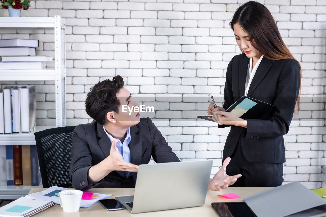 YOUNG WOMAN USING PHONE WHILE STANDING ON LAPTOP