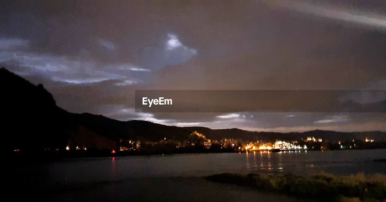 RIVER AMIDST ILLUMINATED CITY AGAINST SKY AT NIGHT