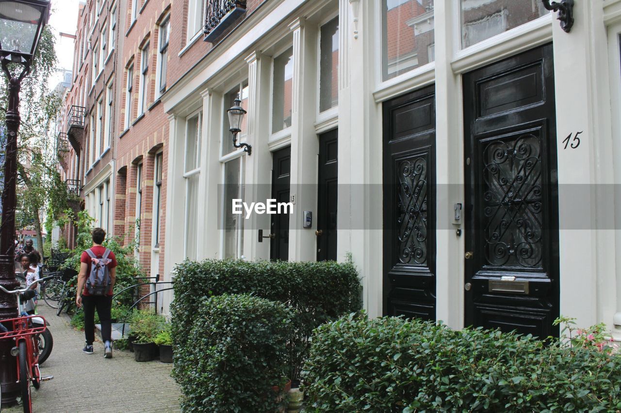 REAR VIEW OF PEOPLE WALKING ON FOOTPATH BY BUILDINGS