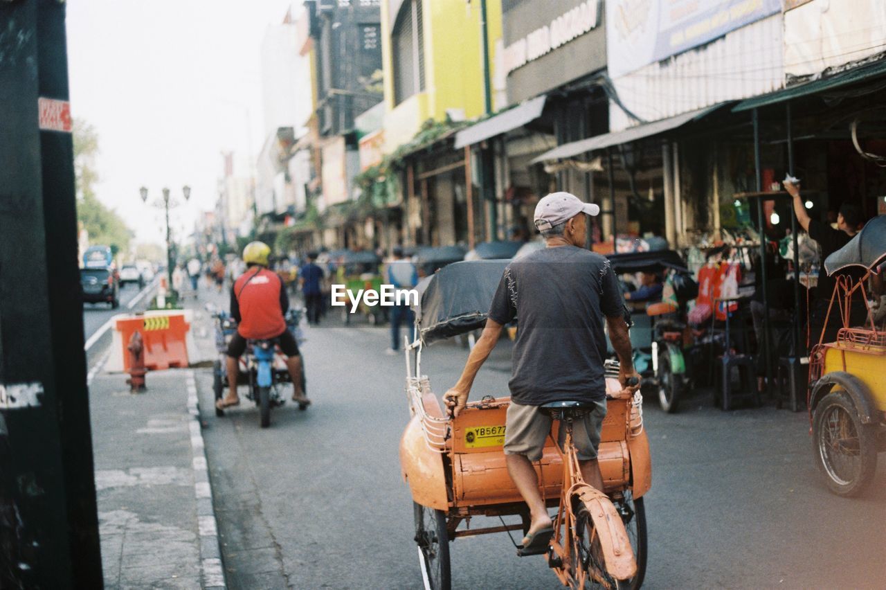 Rear view of man riding pedicab on city street