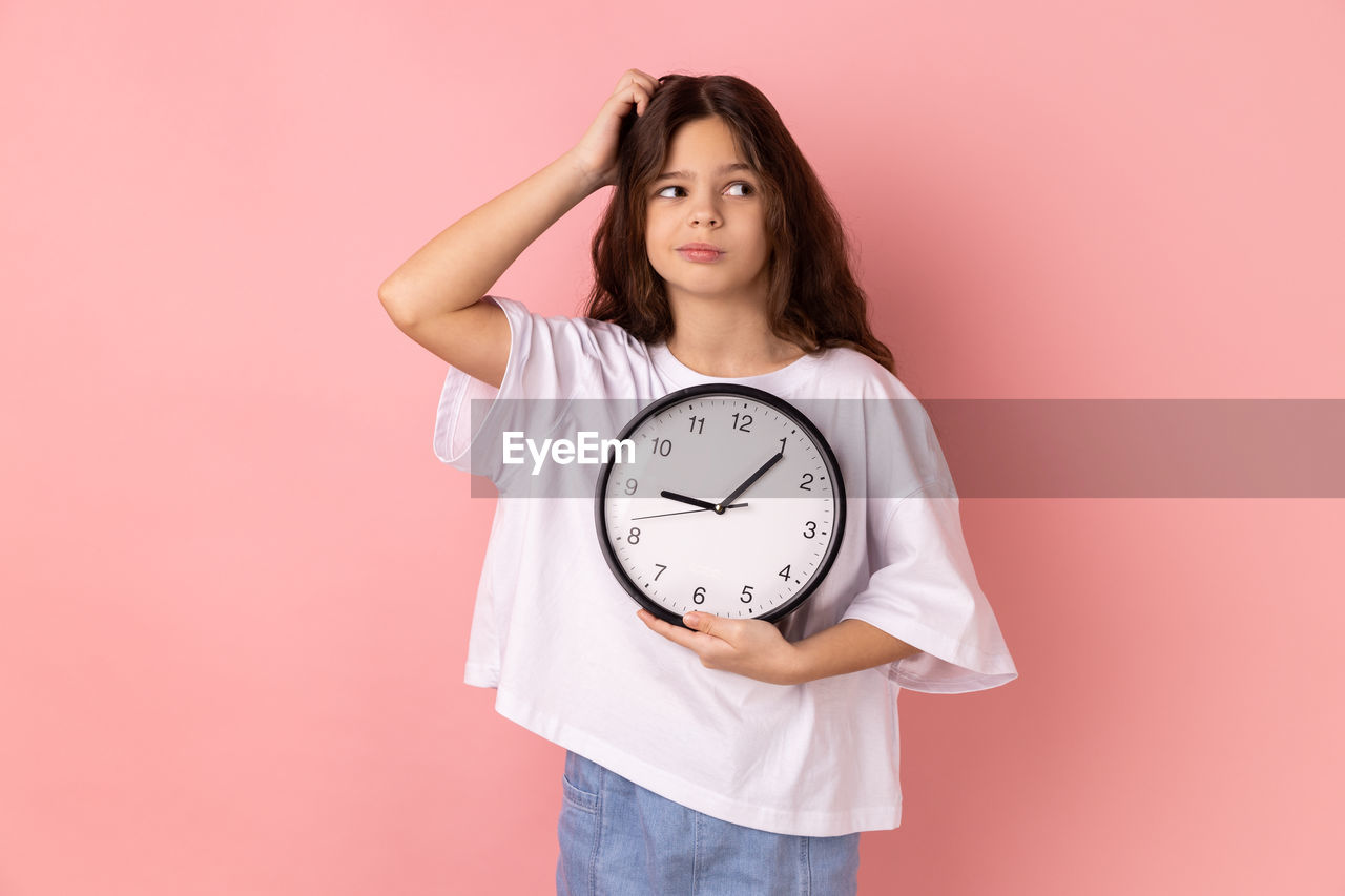 portrait of young woman holding alarm clock against pink background