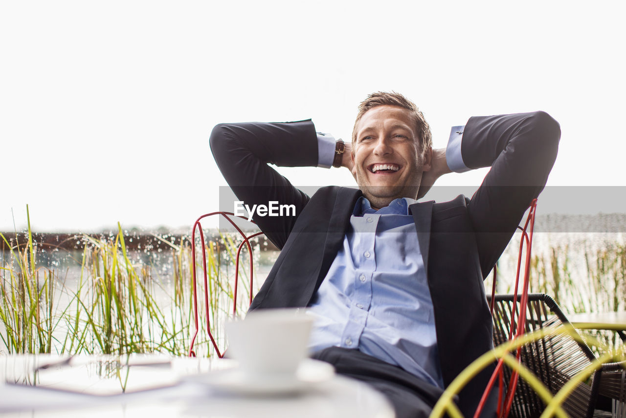 Happy businessman relaxing at outdoor cafe against clear sky