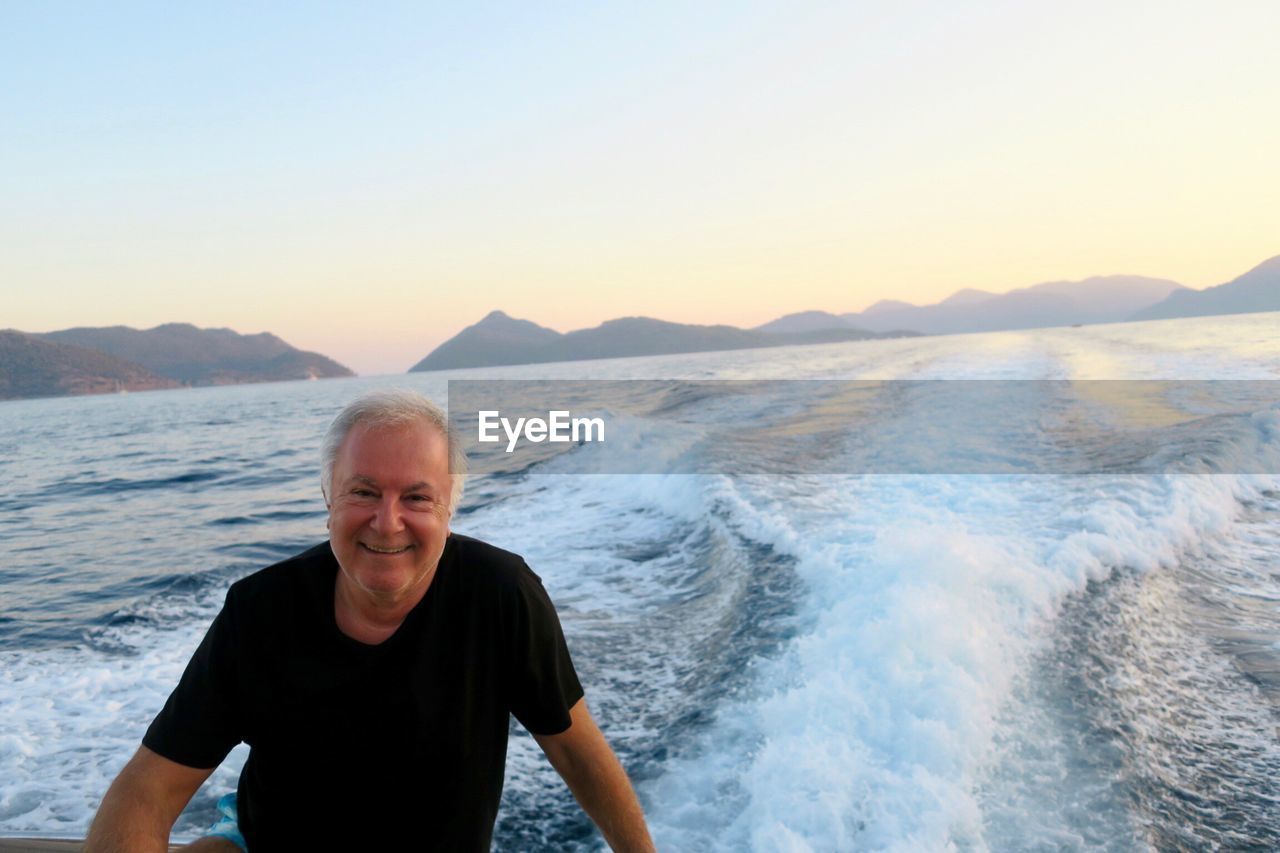 Portrait of smiling senior man standing against sea during sunset