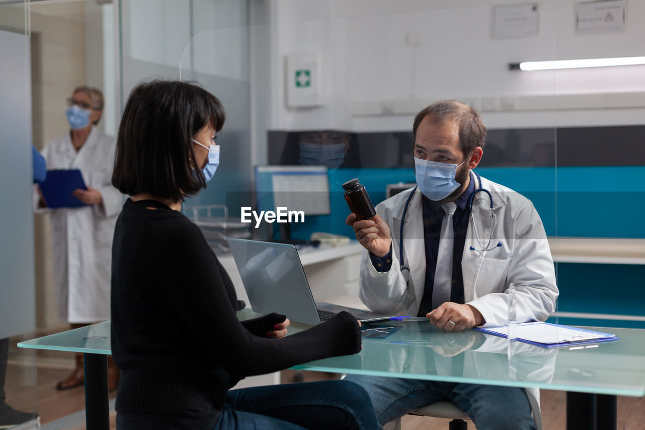 Doctor wearing mask showing medicine to patient