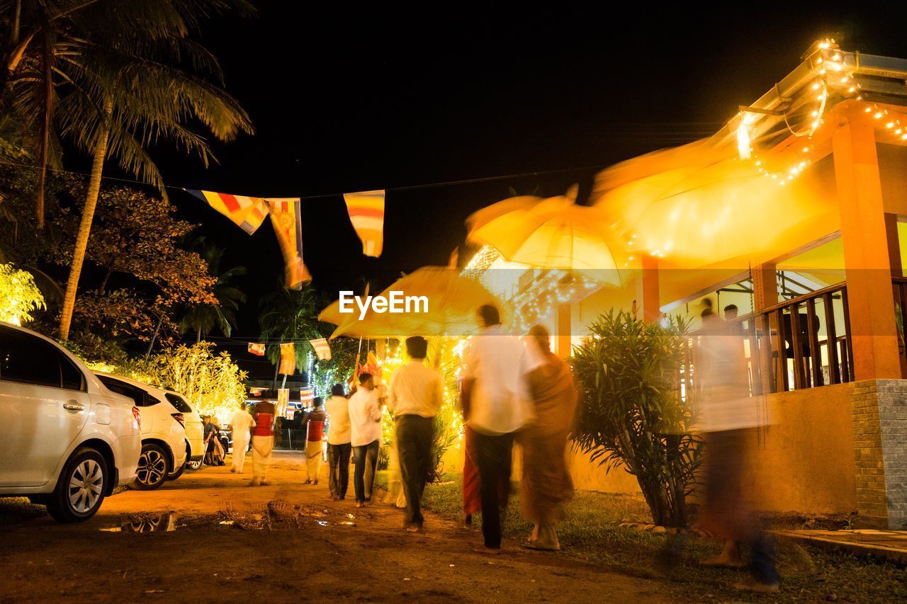 PEOPLE ON ILLUMINATED STREET AT NIGHT IN CITY