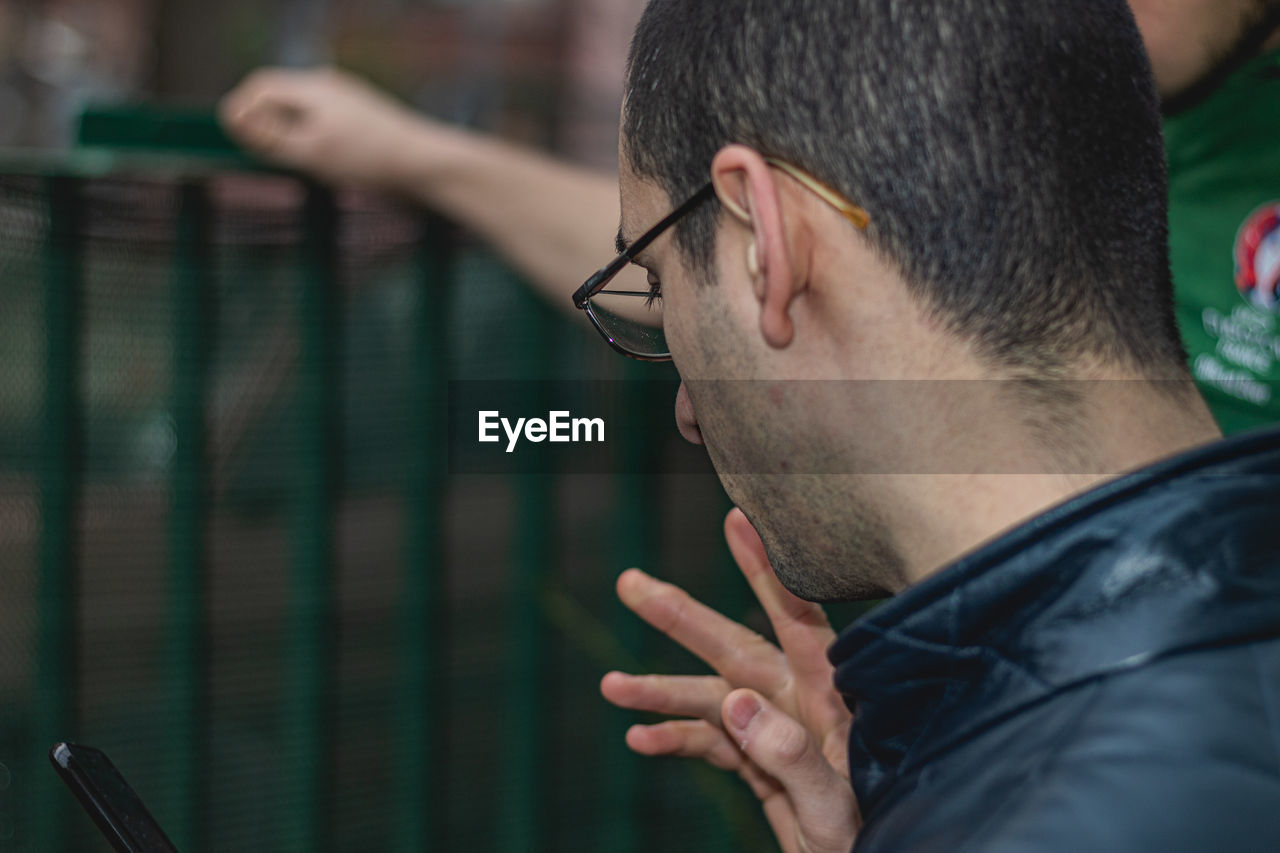 CLOSE-UP PORTRAIT OF YOUNG MAN HOLDING EYEGLASSES