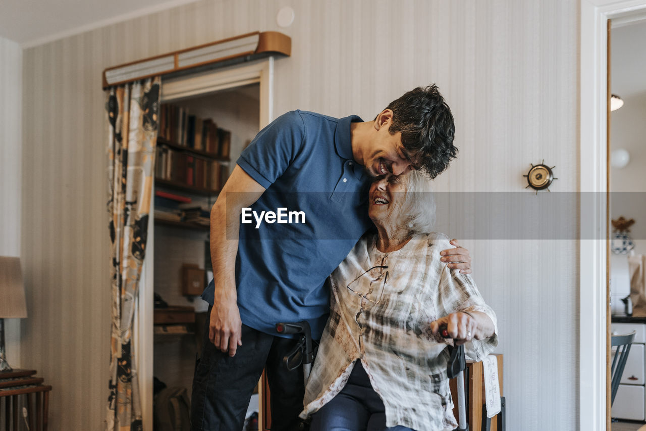 Happy male caregiver embracing senior woman at home