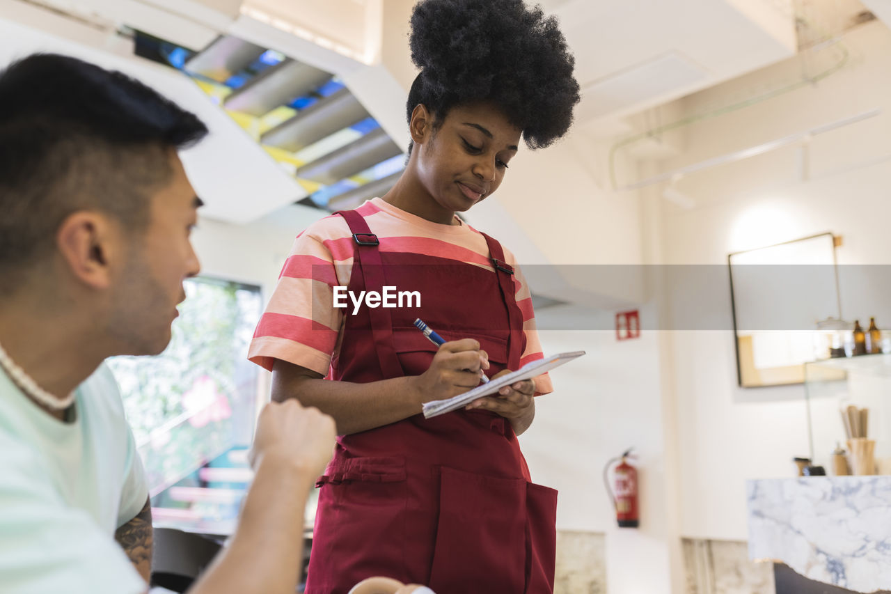 Young waitress taking order from customer in cafe