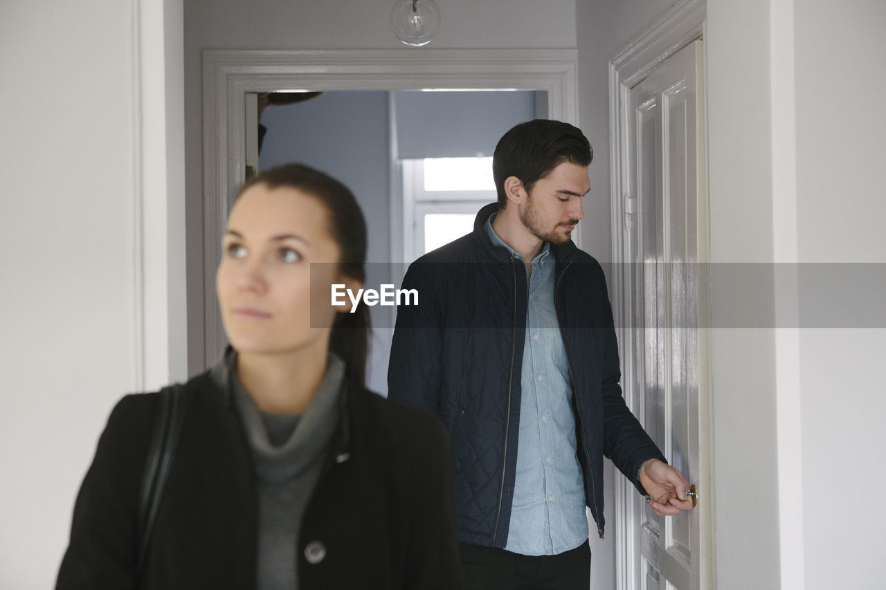 Young man looking at door while standing with woman in corridor