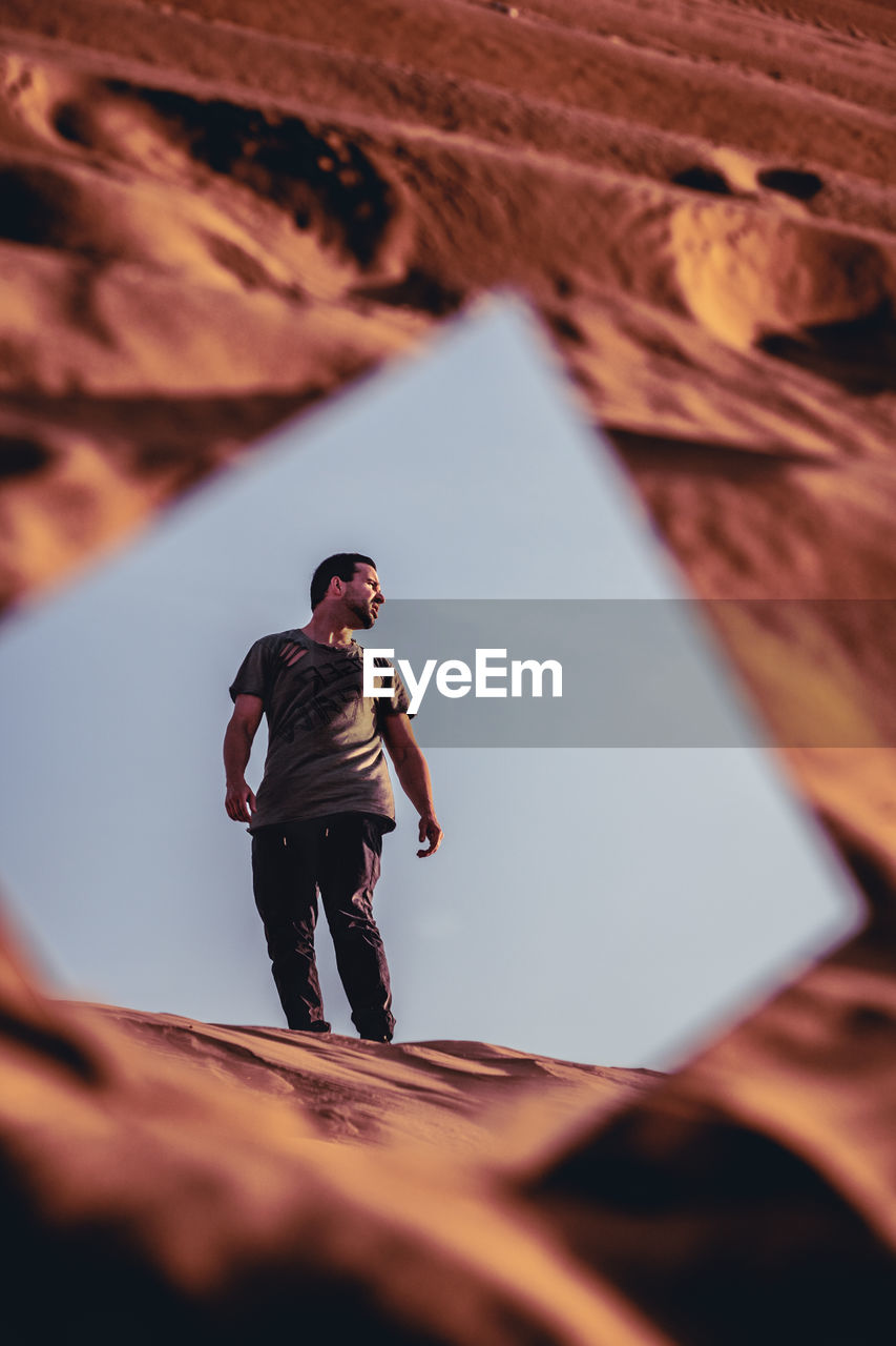 Reflection of man standing on sand in mirror